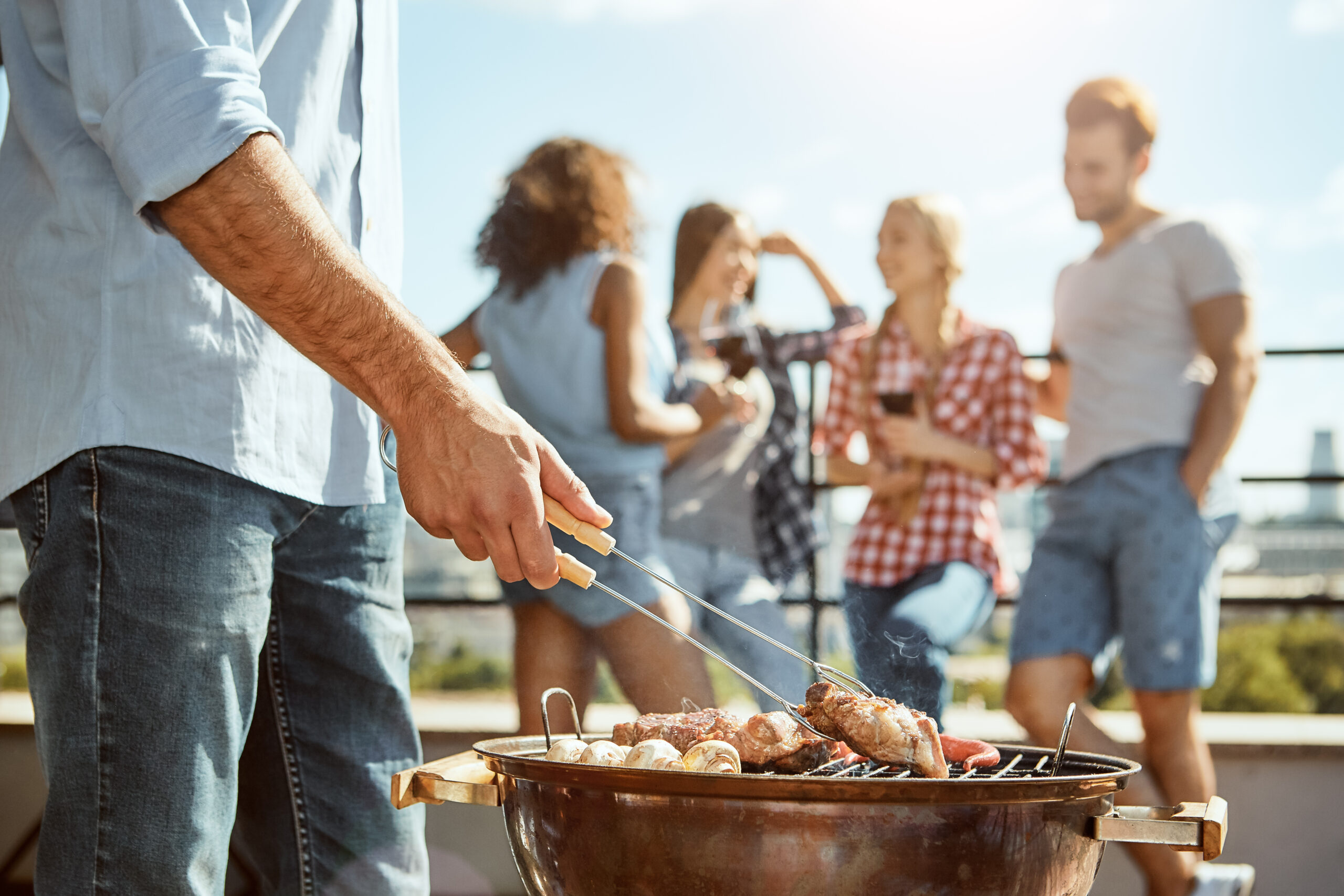 Barbeque time. Man barbecuing meat on the grill while standing on the roof with friends.